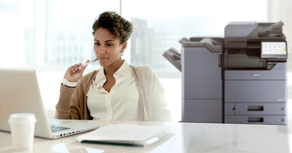 Woman looking at a laptop with printer behind her